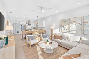 A modern living room with a white sofa, a coffee table, and a dining area with chairs and a table. - The Lighthouse | Ocean and Pool Views, Game Room, Pool + Dock Access (Islamorada)