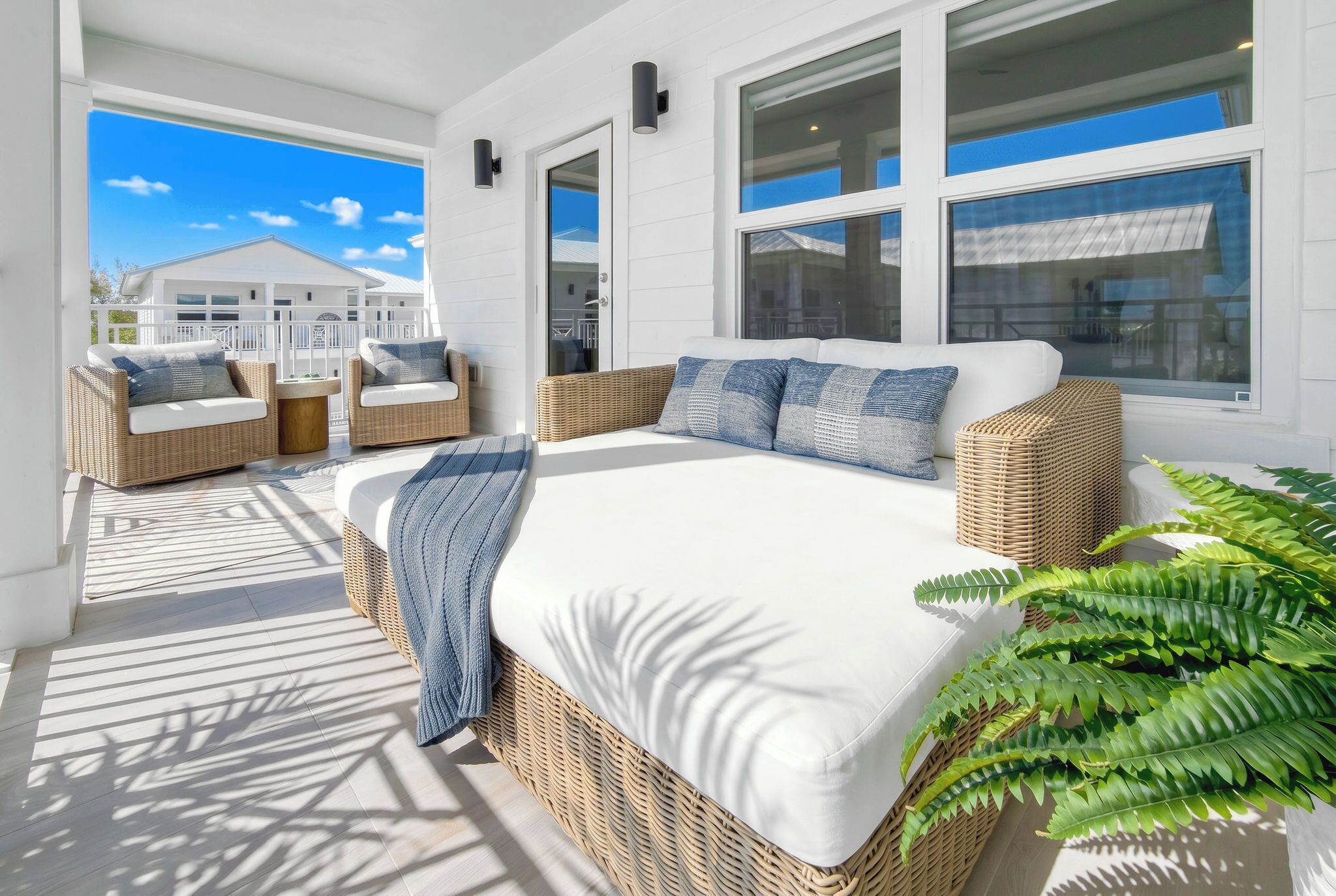 A sunlit room with a large bed, wicker furniture, and a view of a white building.