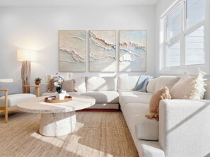 A modern living room with a white sofa, a round coffee table, and abstract wall art.