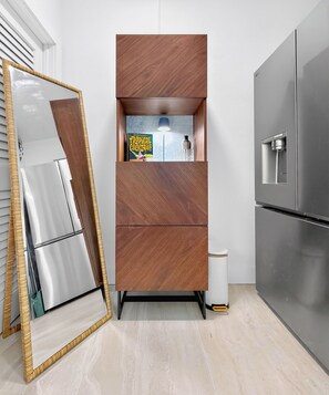 A modern kitchen with a built-in wooden cabinet, a stainless steel refrigerator, and a trash bin.