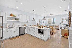 A modern kitchen with white cabinetry, a central island, and a dining area with a view. - The Lighthouse | Ocean and Pool Views, Game Room, Pool + Dock Access (Islamorada)