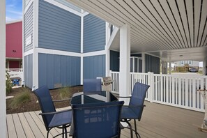 A covered patio with a glass table and chairs, a grill, and a white fence. - Pelican Parade: Ocean View, Pet-Friendly 5 Bedroom Luxury Retreat with Private Pool and Elevator (Oak Island)