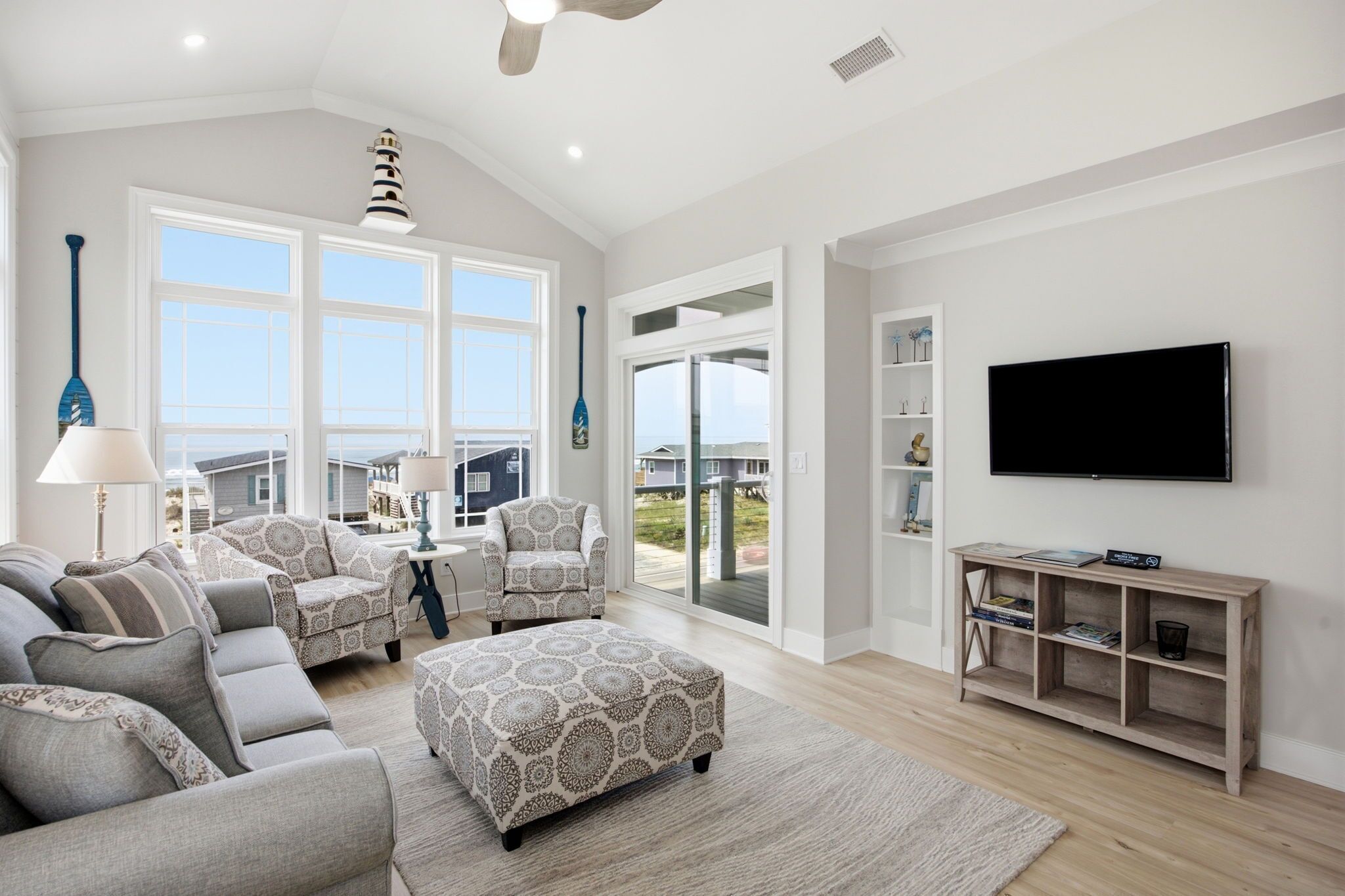A spacious living room with a large sofa, ottoman, and a flat-screen TV mounted on the wall.