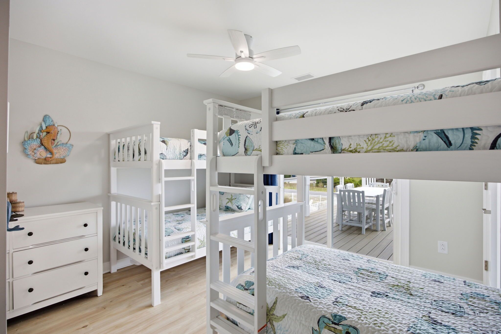 A bunk bed room with a ceiling fan, a dresser, and a decorative seahorse wall art.