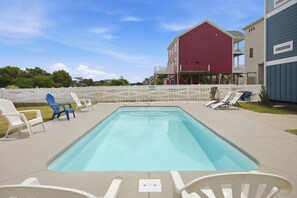 A swimming pool with lounge chairs, a white fence, and a red building in the background. - Pelican Parade: Ocean View, Pet-Friendly 5 Bedroom Luxury Retreat with Private Pool and Elevator (Oak Island)