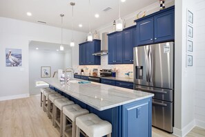 Eine moderne Küche mit einer zentralen Kochinsel, Barhocker, Edelstahlgeräten und blauen Schränken.