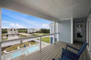 A covered outdoor area with a pool, chairs, and a view of neighboring houses. - Pelican Parade: Ocean View, Pet-Friendly 5 Bedroom Luxury Retreat with Private Pool and Elevator (Oak Island)