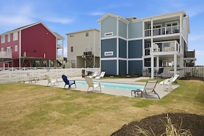 A residential area with a swimming pool, multiple houses, and outdoor seating. - Pelican Parade: Ocean View, Pet-Friendly 5 Bedroom Luxury Retreat with Private Pool and Elevator (Oak Island)