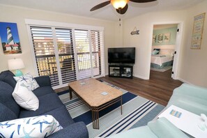 A living room with a sofa, coffee table, TV, and a view through a sliding door. - Newly Remodeled Condo Ocean Village Club F26 (St. Augustine)