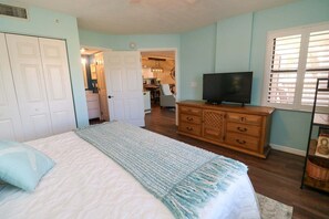Ein Schlafzimmer mit Bett, Kommode, Fernseher und Blick zur Küche.