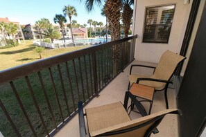 Un balcon avec deux chaises et une table, donnant sur une piscine et des palmiers.