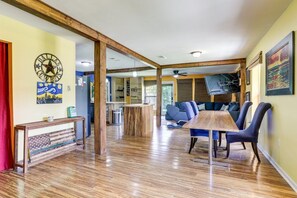 Ein geräumiger Essbereich mit einem Holztisch und Stühlen, im Hintergrund eine Küche und ein Wohnbereich mit Sofa und Fernseher.
