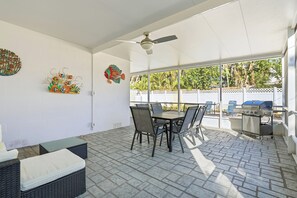 Un patio al aire libre con una mesa, sillas, un ventilador de techo y una parrilla.