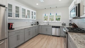 Une cuisine moderne avec des meubles gris, un lave-vaisselle, une cuisinière et une fenêtre donnant sur un espace verdoyant.