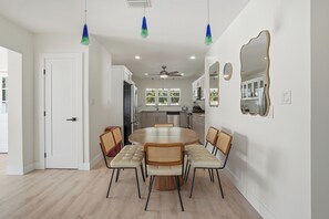 Una cocina moderna con armarios blancos, una mesa redonda con sillas, luces colgantes y un ventilador de techo.