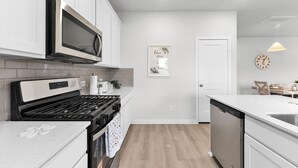 A modern kitchen with white cabinetry, a stainless steel microwave, a gas stove, and a dishwasher. - Brand New 3BR Home with Game Room & BBQ Near The Woodlands (Decker Prarie)
