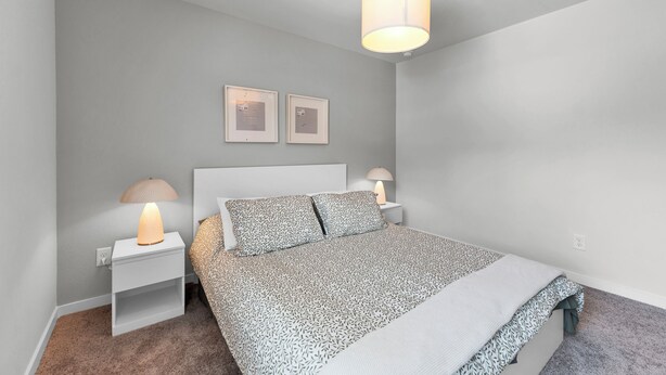 A bedroom with a bed, two bedside tables, a hanging light fixture, and two framed pictures on the wall. - Brand New 3BR Home with Game Room & BBQ Near The Woodlands (Decker Prarie)