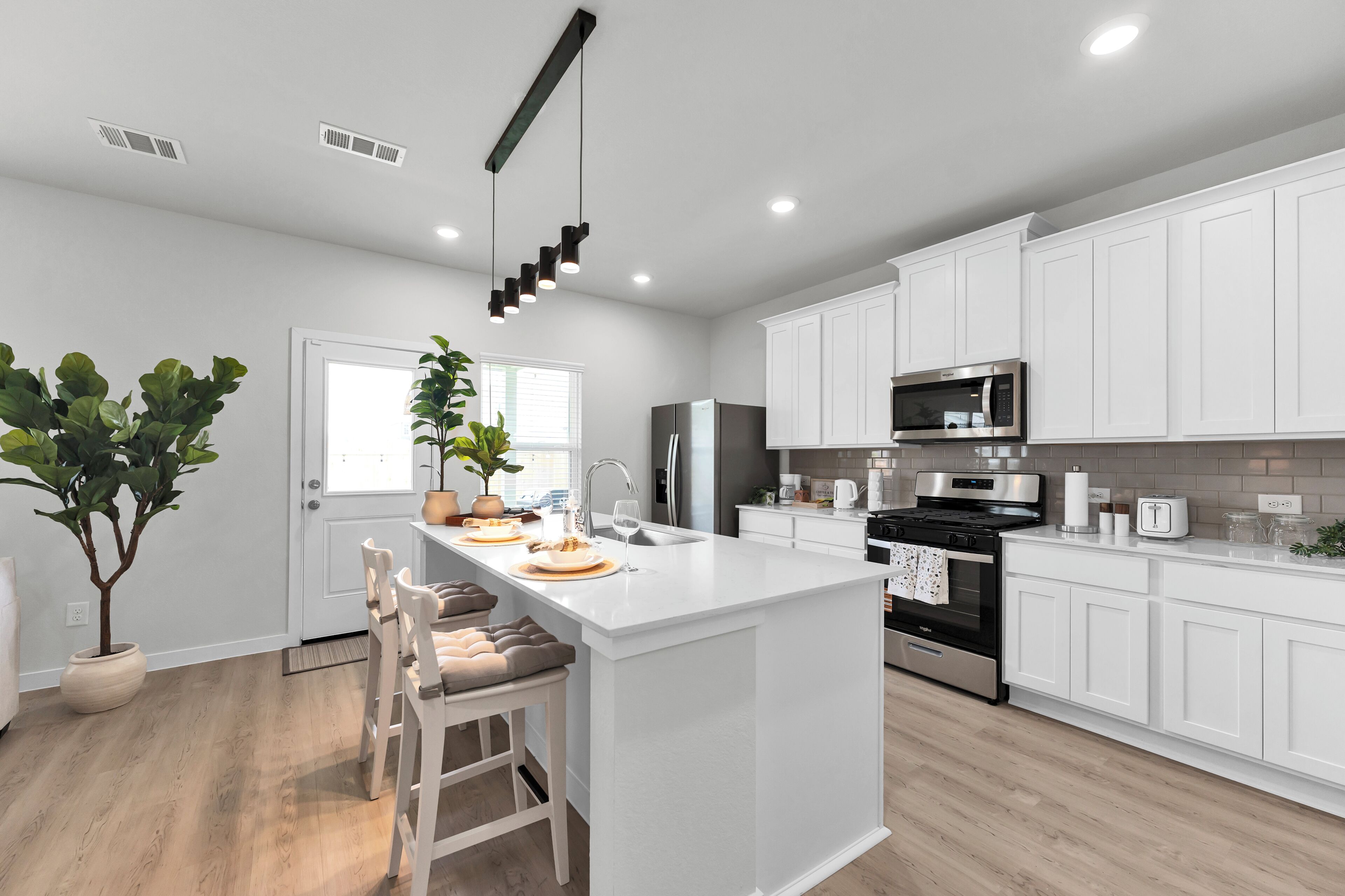 Una cocina moderna con armarios blancos, una isla central, electrodomésticos de acero inoxidable y una lámpara colgante.