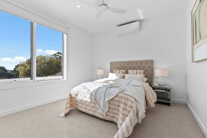 A bedroom with a bed, two bedside tables, a ceiling fan, and a window with a view of trees.