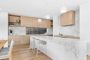 A modern kitchen with marble countertops, wooden cabinets, and pendant lighting.