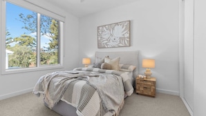 A bedroom with a bed, bedside lamps, a window, and a wall-mounted artwork.