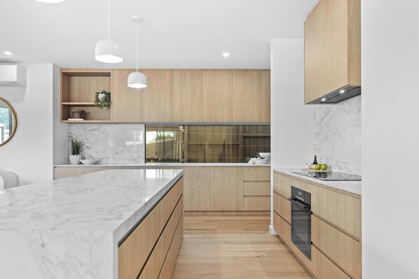A modern kitchen with marble countertops, wooden cabinetry, and pendant lighting.