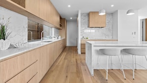 A modern kitchen with wooden cabinets, marble countertops, and a central island with bar stools.