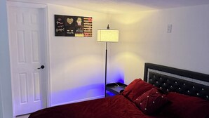 Quarto com cama, mesa de cabeceira, luminária, porta e parede decorada com pôsteres motivacionais.