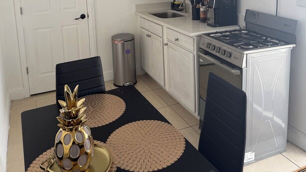Uma cozinha compacta com armários brancos, uma pia de aço inoxidável, um micro-ondas preto e um fogão a gás.