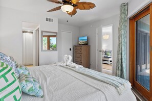 A bedroom with a bed, a ceiling fan, a TV, a dresser, and a view of the outdoors. - La Mirage 102: Spacious 3-bedroom condo in Port Aransas, perfect for family getaways! (Port Aransas)