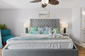 A bedroom with a tufted headboard, a bed with patterned bedding, two bedside lamps, and a ceiling fan. - La Mirage 102: Spacious 3-bedroom condo in Port Aransas, perfect for family getaways! (Port Aransas)