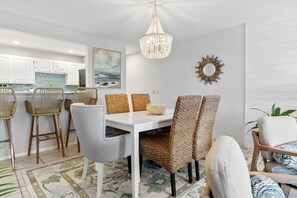 A dining area with a white table, wicker chairs, and a chandelier. - La Mirage 102: Spacious 3-bedroom condo in Port Aransas, perfect for family getaways! (Port Aransas)