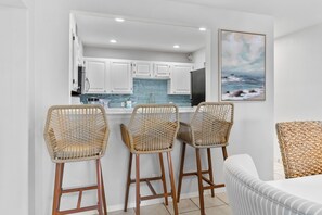 A kitchen with white cabinets, a blue backsplash, and a painting of a beach scene. - La Mirage 102: Spacious 3-bedroom condo in Port Aransas, perfect for family getaways! (Port Aransas)