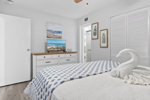 Une chambre à coucher avec un lit, une commode, un téléviseur et une porte.