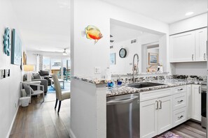 A modern kitchen with white cabinetry, a granite countertop, and a stainless steel dishwasher. - Enjoy stunning partial Gulf views from La Mirage 301 in Port Aransas, TX. (Port Aransas)