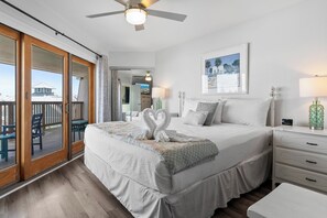 Een hotelkamer met een groot bed, een plafondventilator, uitzicht door de schuifdeur, een nachtkastje en een bijzettafeltje.