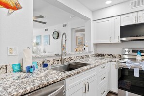 A modern kitchen with white cabinetry, a marble countertop, and stainless steel appliances. - Enjoy stunning partial Gulf views from La Mirage 301 in Port Aransas, TX. (Port Aransas)