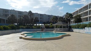 En swimmingpool med ett lusthus, omgiven av palmer och en hög byggnad i bakgrunden.