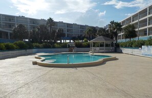 Ein Swimmingpool mit einem Gazebo, umgeben von Palmen und einem mehrstöckigen Gebäude im Hintergrund.