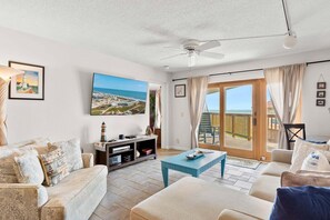 A living room with a sofa, a coffee table, a TV, and a large window with a view of the sea. - Discover La Mirage 224: a cozy 2-bedroom condo with partial Gulf views in Port Aransas. (Port Aransas)