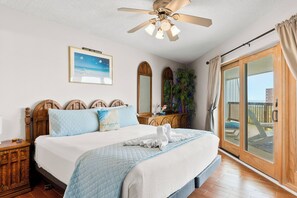 A bedroom with a bed, a ceiling fan, a large window, and a view of the outdoors. - Discover La Mirage 224: a cozy 2-bedroom condo with partial Gulf views in Port Aransas. (Port Aransas)