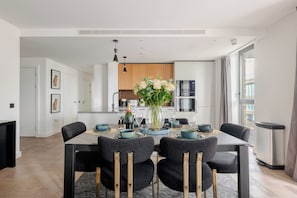 Un espace repas moderne avec une table rectangulaire, des chaises noires aux pieds dorés et un vase rempli de fleurs.