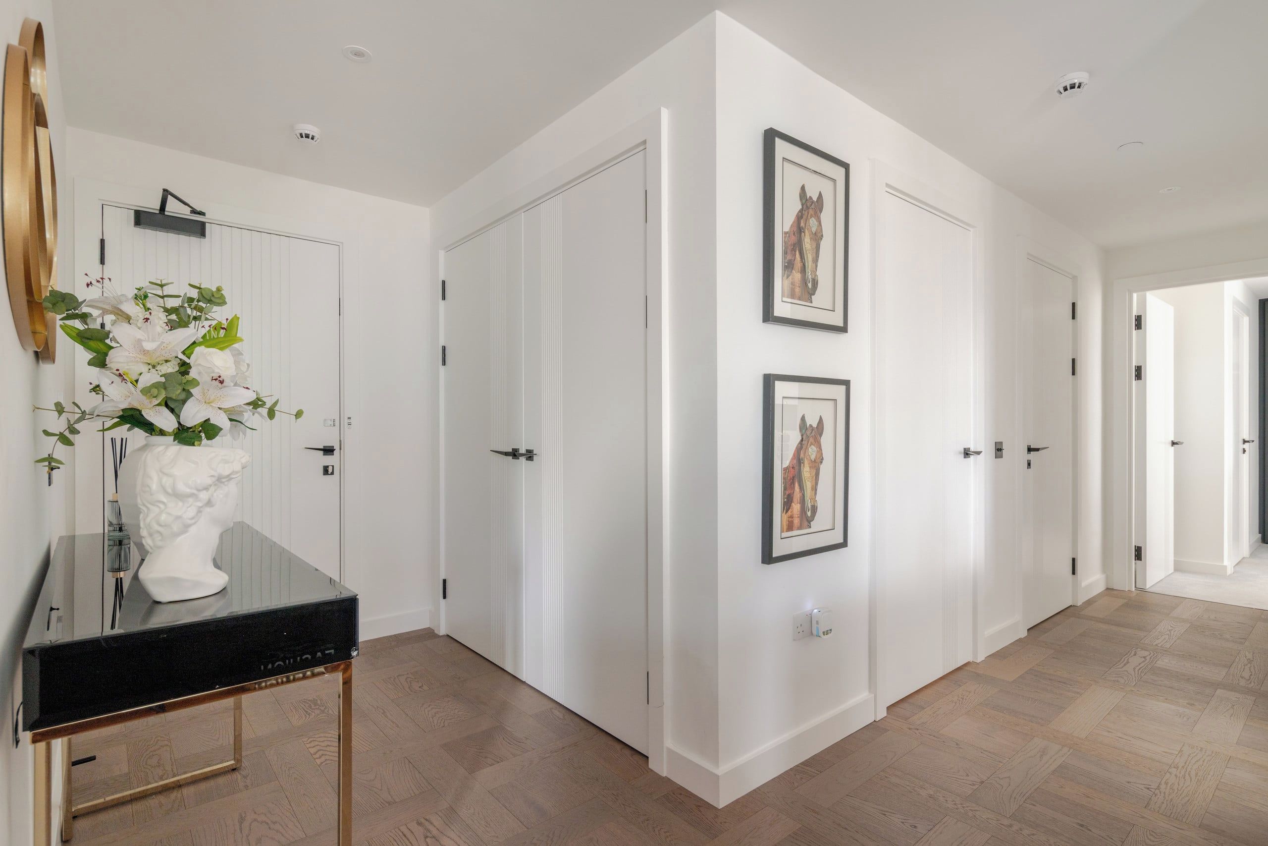 A hallway with white doors, a black console table with a vase of flowers, and two framed pictures on the wall.