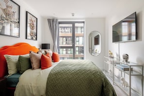 A modern bedroom with a large bed, a television, a mirror, and artwork on the walls. - The London Dock HQ - 3 Bed with AC for 6 Guests (London)