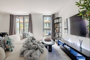 A modern living room with a sofa, a large fluffy throw, a coffee table, a TV, and a bookshelf. - The London Dock HQ - 3 Bed with AC for 6 Guests (London)