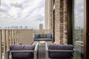 A balcony with a sofa and two armchairs, a wooden table, and a cityscape view. - The London Dock HQ - 3 Bed with AC for 6 Guests (London)
