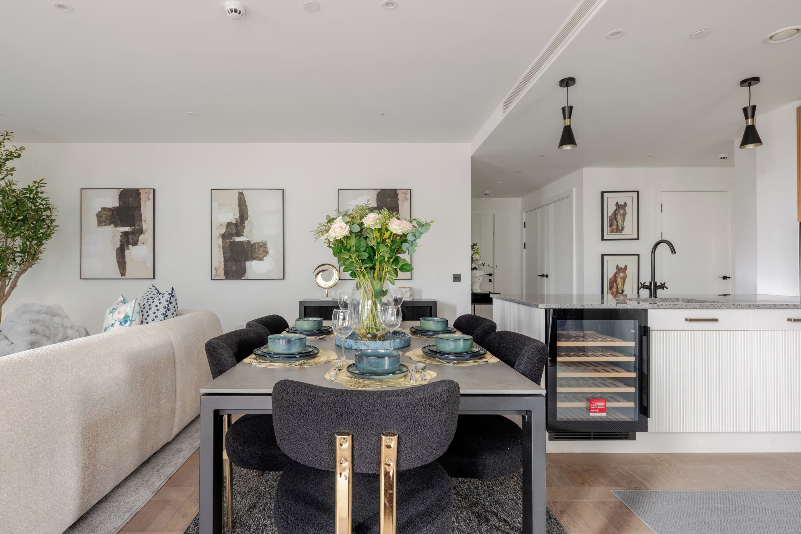 A modern dining area with a table set for six, surrounded by dark chairs, a vase with flowers, and abstract wall art.