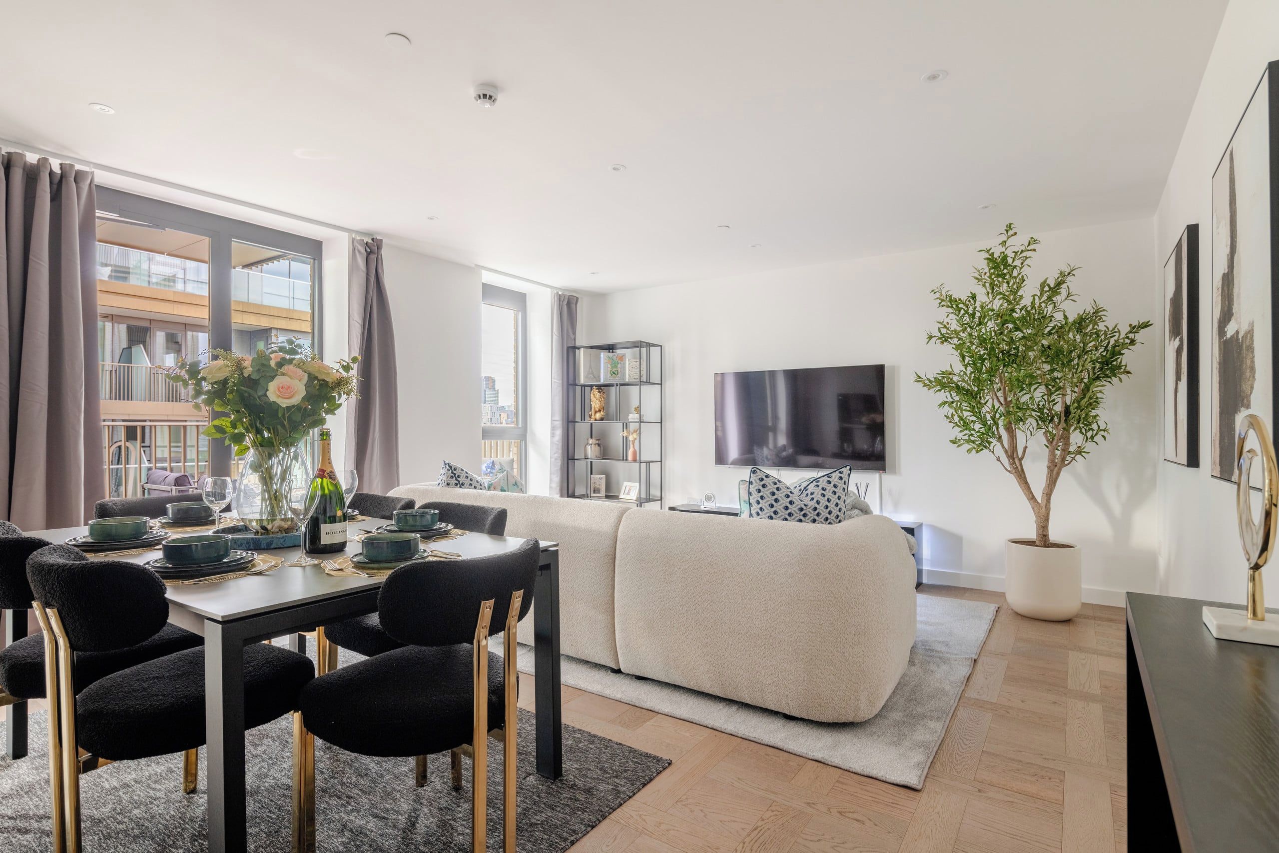 A modern living room with a dining area, a flat-screen TV, and a large window with curtains.