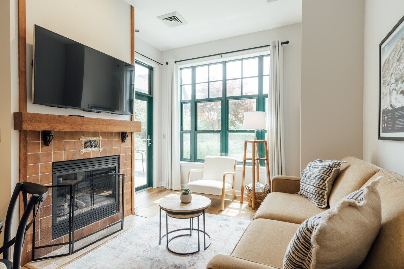 A living room with a fireplace, a television mounted above it, a sofa, a coffee table, and a large window with curtains.