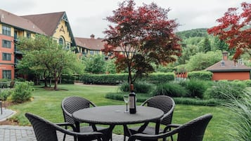An outdoor seating area with wicker chairs and a table, surrounded by well-maintained greenery and a building with a distinctive roof.